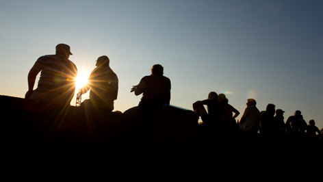 Menschen sitzen auf einer Mauer und betrachten den Sonnenuntergang.