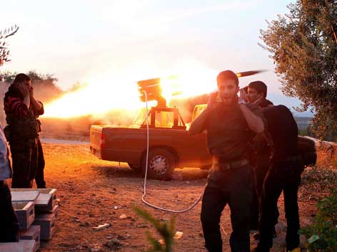 Syrische Kämpfer zünden eine Rakete von einem Lastwagen und halten sich die Ohren zu.