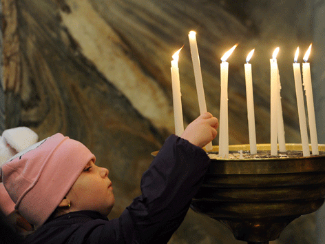Ein Kind steckt eine brennende Kerze in eine Schale