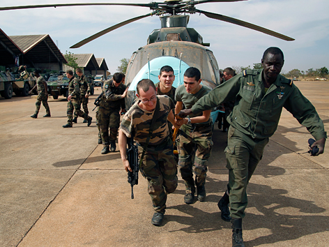 Französische Soldaten helfen malischen Truppen, einen beschädigten Hubschrauber aus dem Hangar zu befördern