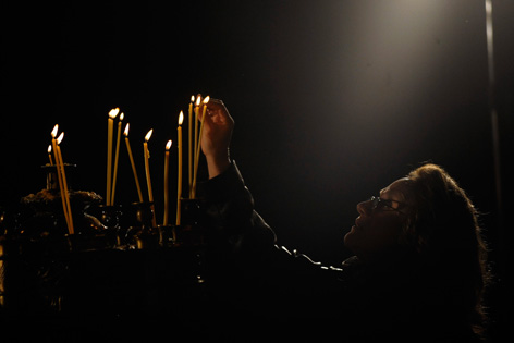 Eine orthodoxe Gläubige zündet im Dunklen eine Kerze an