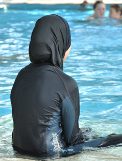 Muslimisches Mädchen in einem Burkini sitzt am Rand eines Schwimmbeckens
