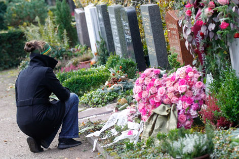 Eine Frau kniet bei einem Grab. Im Hintergund viele Gabsteine