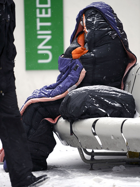 Obdachloser im Winter. Sitzt in der Kälte auf einer Bank