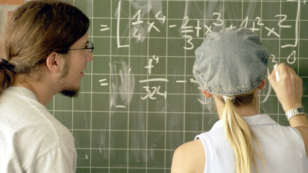 Ein junger Mann und eine junge Frau vor einer Tafel mit mathematischen Formeln