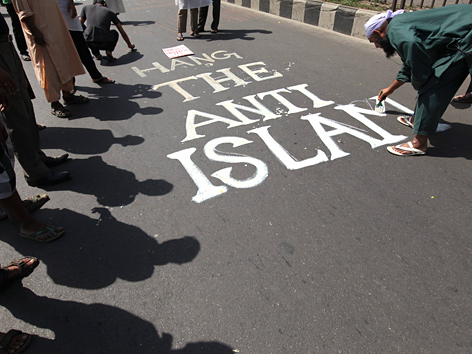 Mann pinselt Slogan "Hang the Anti-Islam" auf eine Straße in Dhaka, Bangladesch
