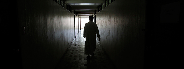 Silhouette eines Priesters, der einen dunklen Gang entlang geht
