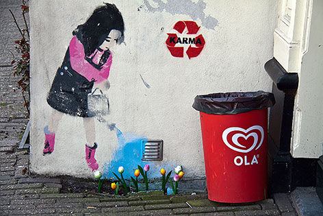 Wandmalerei auf einem Haus in Amsterdam: Ein Mädchen mit Gießkanne, vor dem Haus wachsen Tulpen, der Wasserstrahl der Gießkanne fällt genau auf die Tulpen