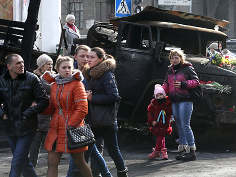 Menschen in Kiew gehen an einem ausgebrannten Militärfahrzeug vorbei