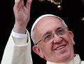 Papst Franziskus winkt vom Balkon, im Hintergrund ein großes geschmücktes Kreuz