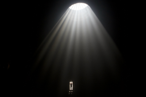 Silhouette eines Mannes in der Tür eines riesigen dunklen Raums. Licht dringt von oben durch eine runde Öffnung ein.