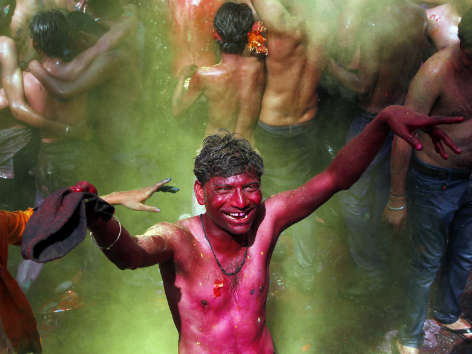 Grün bemalter indischer Mann umgeben von Massen, die mit Farbpulver um sich werfen