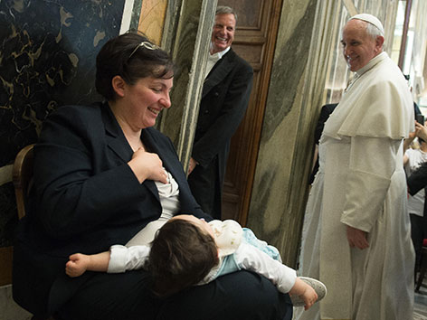 Papst Franziskus geht an einer Frau mit einem Kleinkind am Schoß vorbei