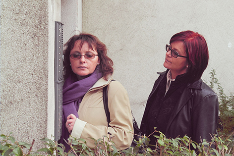 Zwei Frauen horchen vor einer Tür an der Gegensprechanlage