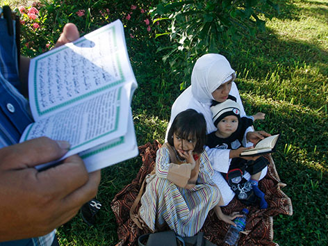 Eine muslimische Familie sitzt in einer Wiese die Eltern lesen im Koran