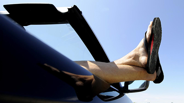 Ein junger Mann streckt seine Beine aus seinem Auto