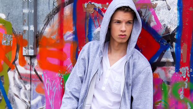 Ein cool blickender Jugendlicher vor einer Graffitiwand