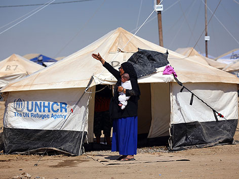 Eine Frau steht mit einem Baby auf dem Arm vor einem Zelt der UNO Flüchtlingsorganisation UNHCR im Norden des Irak
