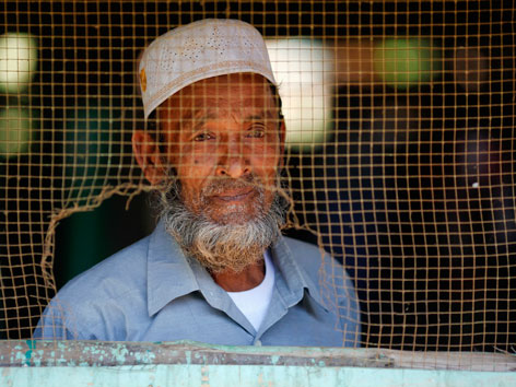 Ein Muslim in Myanmar blickt durch ein Fenster mit Draht in eine Moschee
