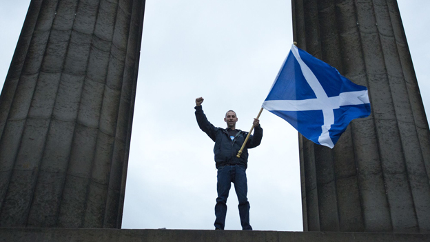Ein Mann schwingt die schottische Flagge auf Scottish National Monument in Calton Hil