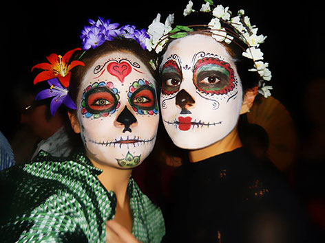 Als bunte Skelette geschminkte Frauen und bunte Altäre zum mexikanischen "Tag der Toten"