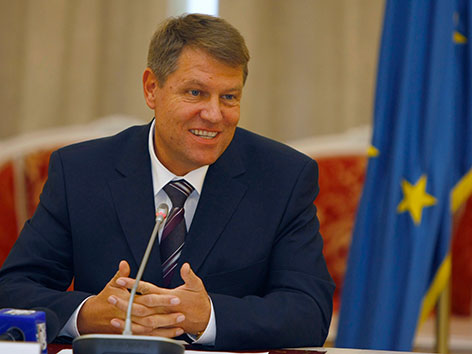 Klaus Johannis, rumänischer Präsident sitzend, lächelnd, mit europäischer Flagge im Bild