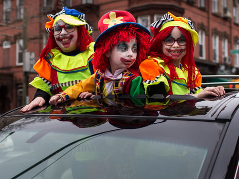 Drei als Clowns verkleidete Kinder schauen aus dem Sonnendach eines Autos (Purim)