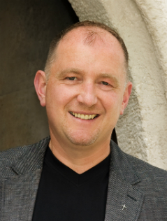 Pfarrer Wolfgang Schnölzer lächelnd unter einem Torbogen