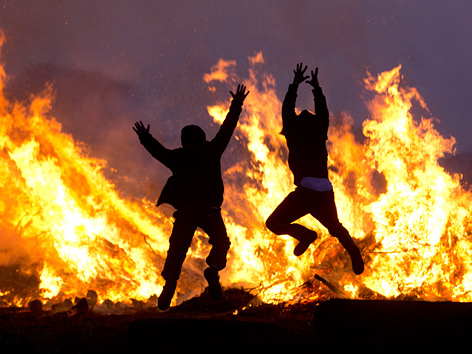 Kinder hüpfen vor einem Osterfeuer