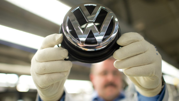 Mitarbeiter hält mit behandschuhten Händen das VW-Logo in die Kamera