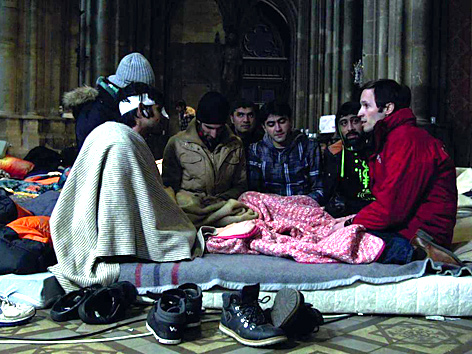 Filmstill "Last Shelter": Flüchtlinge sitzen mit Caritas-Geschäftsführer Klaus Schwertner auf Matratzen in der Wiener Votivkirche