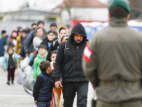 Flüchtlinge in einer Reihe vor einem österreichischen Grenzbeamten