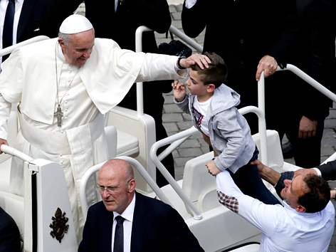 Papst Franziskus streichelt ein Kind, das ihn seinen offenen Wagen gehalten wird