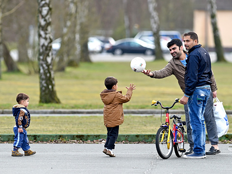 Flüchtlinge, zwei Männer und zwei kleine Kinder mit Fußball und Fahrrädern