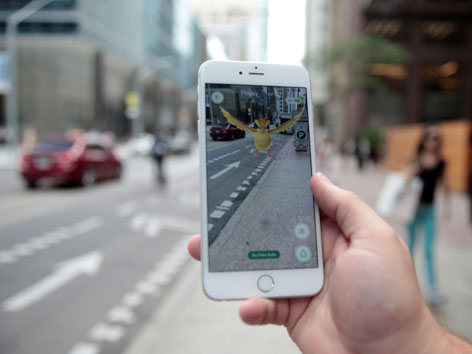 Ein Smartphone, auf dem die dahinterliegende reale Straße in ein Pokemon-Spiel integriert ist.