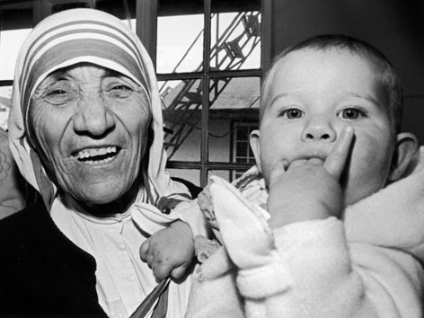 Mutter Teresa lachend mit einem kleinen Kind am Arm