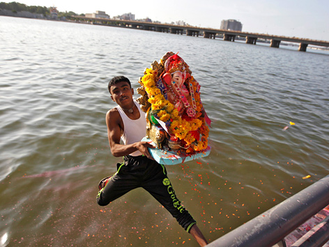 Ein Gläubiger springt mit einer Ganesha-Statue ins Wasser in Ahmedabad, Indien