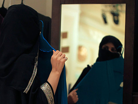 Eine verschleierte Frau probiert einen Nikab vor einem Spiegel an