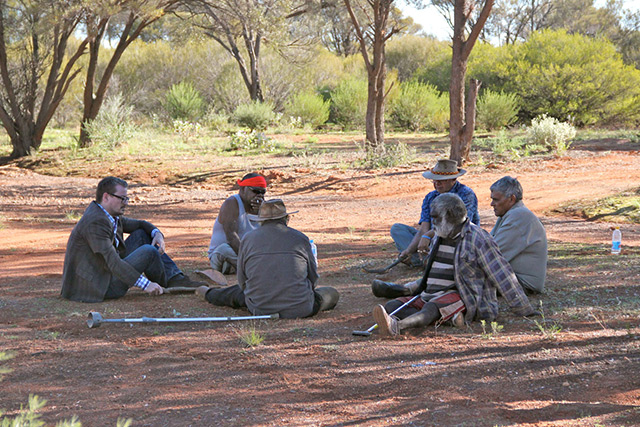 Forscher im Gespräch mit Aborigines, auf dem Lehmboden im Freien sitzend