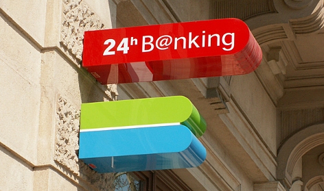 Schilder an einer Bankfiliale verweisen auf 24-Stunden-Banking und einen Bankomat