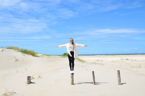 junge Frau am Meer balanciert auf einem Holzpfahl