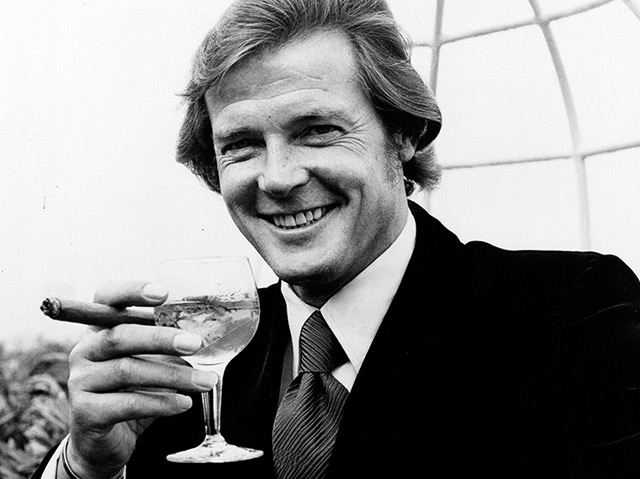 James Bond Darsteller Roger Moore, der 1972 einen Martini und eine Zigarre in der Hand hält