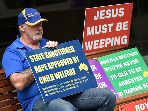 Ein Demonstrant hält Schilder vor der Royal Commission into Institutional Responses to Child Sexual Abuse in Sydney