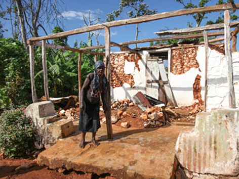 Eine alte Frau auf Haiti steht vor einem zerstörten Haus