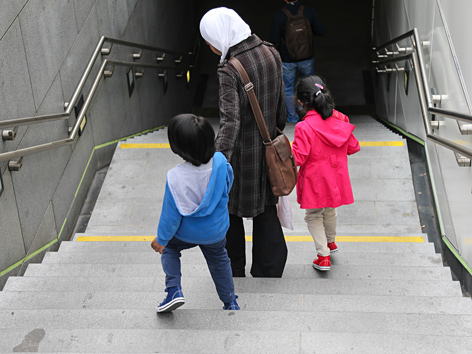 Eine junge Mutter mit Kopftuch und zwei Kindern steigt eine Treppe in die U-Bahn hinunter