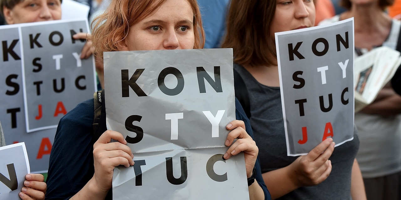 Protesters hold posters reading "constitution" during a protest in front of the presidential palace in Warsaw