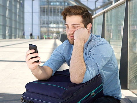 Junger Mann blickt genervt auf sein Smartphone