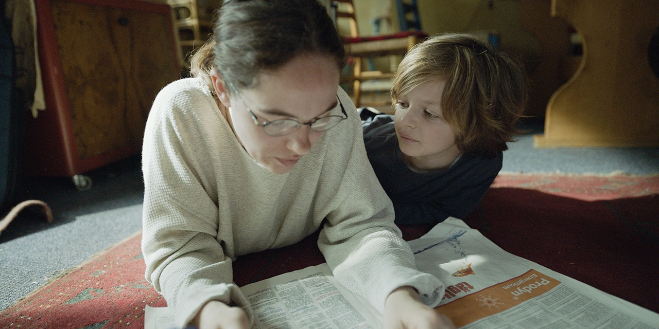 Filmstill "Die beste aller Welten" Kind und Mutter liegen am Boden und lesen Zeitung