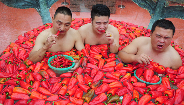 Drei Männer sitzen in einem Pool mit schwimmenden Paprikaschoten und essen Chilis