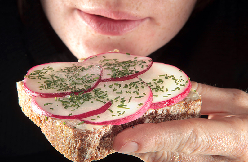 Eine Frau hält ein Brot belegt mit Radieschen und Schnittlauch